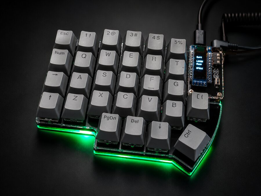 Left half of a gray Lily58 on a dark background, with the OLED screen on and green light under the case